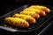 mustard coated sausages sizzling on a black grill plate