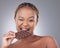 My sneaky snack. Studio shot of an attractive young woman eating a slab of chocolate against a grey background.