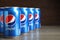 MYKOLAIV, UKRAINE - FEBRUARY 9, 2021: Many cans of Pepsi on wooden table, space for text