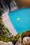 Myrtos Beach, Kefalonia Island, Greece. Figure of a parachutist skydiver with orange parachute against a blue lagoon bay