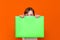 Mysterious caucasian young girl hiding under bright green folder with a banner advertisement on a orange