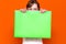 Mysterious caucasian young girl hiding under bright green folder with a banner advertisement on a orange