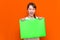 Mysterious caucasian young girl hiding under bright green folder with a banner advertisement on a orange