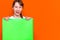 Mysterious caucasian young girl hiding under bright green folder with a banner advertisement on a orange