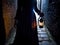 Mysterious figure holding glowing hourglass in alleyway