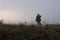 A mysterious figure wearing a fedora hat, standing out of focus in a field in the background on a misty winters day