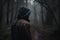 Mysterious foggy forest with silhouette of a man in hood