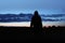 A mysterious hooded figure, back to camera. Silhouetted, looking at the sunset