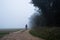 A mysterious hooded figure, back to camera. Standing on a track by woodland, on a spooky, misty autumn day