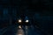 A mysterious hooded man, back to camera. Standing in front of car headlights. On a country lane at night