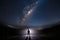 A mysterious man standing in the middle of the road looking into bright light with milky way starry night sky