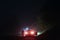 A mysterious man standing next to a car on a spooky empty road on a foggy night. Silhouetted by street lights.