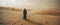 a mysterious person standing in the desert with sand blowing in the background