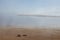 Mysterious shore of sea in early morning in calm weather with soft haze above water and yellow sand beach in mist.