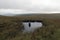 A mysterious silhouette of a man reflected in water with no one above on a bleak moorland hillside