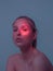 Mysterious studio portrait of young girl with red neon light spot on her eye and naked shoulders