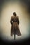 mysterious woman wearing trench coat and pulled back hair walking down a foggy 20th century city.