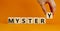 Mystery symbol. The concept word Mystery on wooden cubes. Beautiful orange table, orange background, copy space. Businessman hand