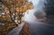 Mystical autumn foggy forest with road. Fall misty woods
