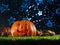 Mystical Halloween composition. Smiling halloween pumpkin with illuminated carved face, autumn fruits, cones on a green lawn