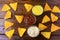 Nachos corn chips spread on wooden table next to assorted sauces. Top view