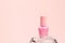 Nail polish small glass bottle on crystal podium on light pink background. Unbranded mockup with copy space, front view, template