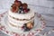 Naked cake with caramelized fruits - strawberries, blueberries, raspberries. Sponge cream cake in floral high plateau, tray.