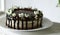 Naked drip cake with chocolate, decorated with strawberries, jasmine flowers and honeysuckle on white wooden table