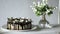 Naked drip cake with chocolate, decorated with strawberries, jasmine flowers and honeysuckle on white wooden table