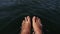 Naked hairy male legs hang from a catamaran. The legs of a man swim towards the waves on a ship. First person of view