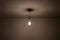 Naked lit light bulb hanging from the ceiling of a dimly lit room