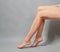 Naked long female legs sitting on a chair. Foot massage. Gray background. Side view