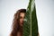 Naked woman hiding face behind big green leaf.