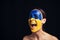Naked young woman with painted Ukrainian flag on face screaming isolated on black