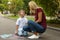 Nanny with cute little boy drawing house with chalks