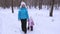 Nanny leads hand of little girl on snowy road while walking in fresh air in park in winter. Mom and daughter make first