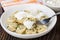 Napkin, bowl with sour cream, dumpling strung on fork in plate with dumplings on wooden table