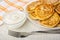 Napkin, bowl with sour cream, white dish with cottage cheese pancakes, fork on wooden table