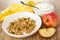 Napkin, bowl with yogurt, spoon, granola in plate, whole apple and piece of apple on table