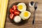 Napkin, brown plate with pieces of tomato, bowl of mayonnaise, fried eggs, salt, fork on wooden table. Top view