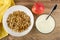 Napkin, granola in plate, apple, spoon in bowl with yogurt on wooden table. Top view