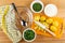 Napkin, spoon in bowl, bowls with dill, scallion, bowl with sour cream, baked potatoes, knife on cutting board on table. Top view