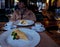 Napoleon cake on a white ceramic plate and coffee cups, glasses with unfinished white wine and a pretty mature woman looking out