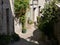 Narrow alley in semi-shade, southern France,Pot and tub plants, typical sandstone for houses, coarse cobblestones, pipes for