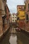 Narrow canal with moored boats between residential buildings in non-touristic part of Venice, Italy. Cityscape in rainy day