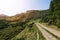 Narrow car gravel road in the mountains leading up and illuminated by the sun`s rays