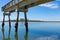 Narrow concrete fishing pier with oyster and barnacle covered pilings, blue sky reflected in still waters, Tybee Island Georgia US