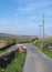 a narrow country lane with wooden electricity poles and lines in a sunlit rural landscape on the old howarth road in calderdale