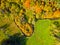 Narrow creek meanders in autumnal landscape from above