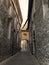 A narrow, deserted street in Como, Italy, leading between old stone houses. Small bridge connecting the houses above street level